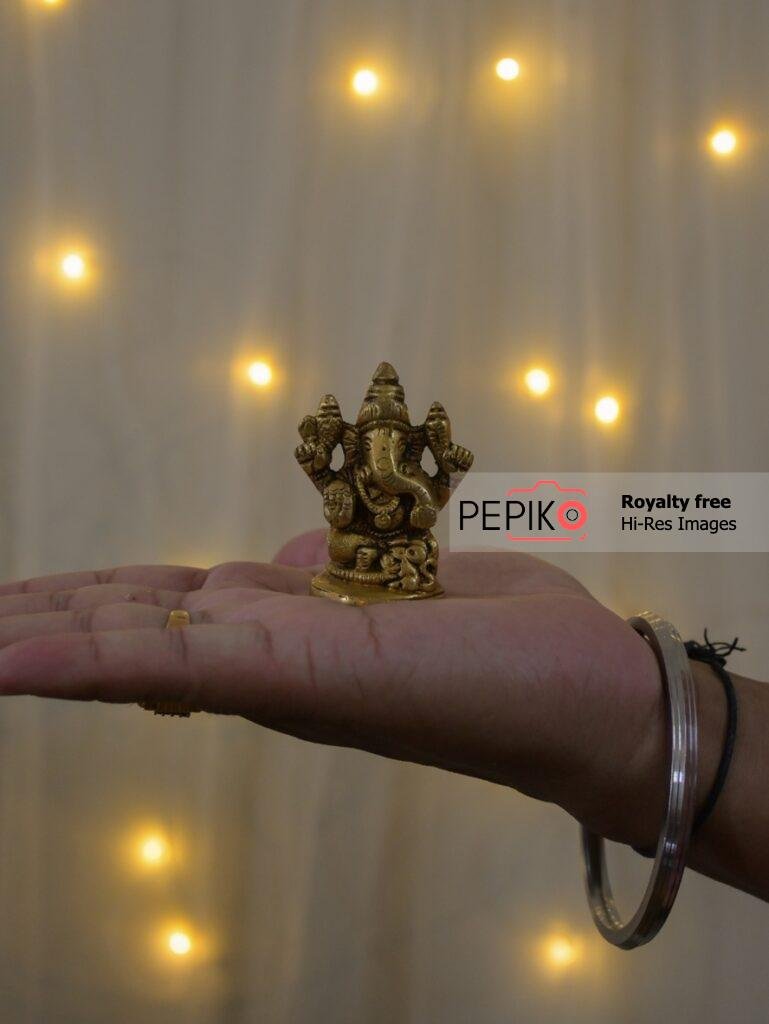 
									Close up of Lord Ganesh small statue on men palm.